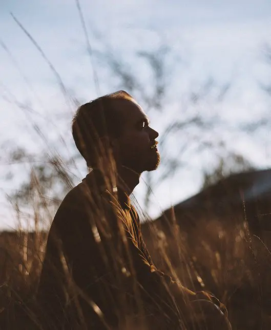 A man standing in tall grass looking up.