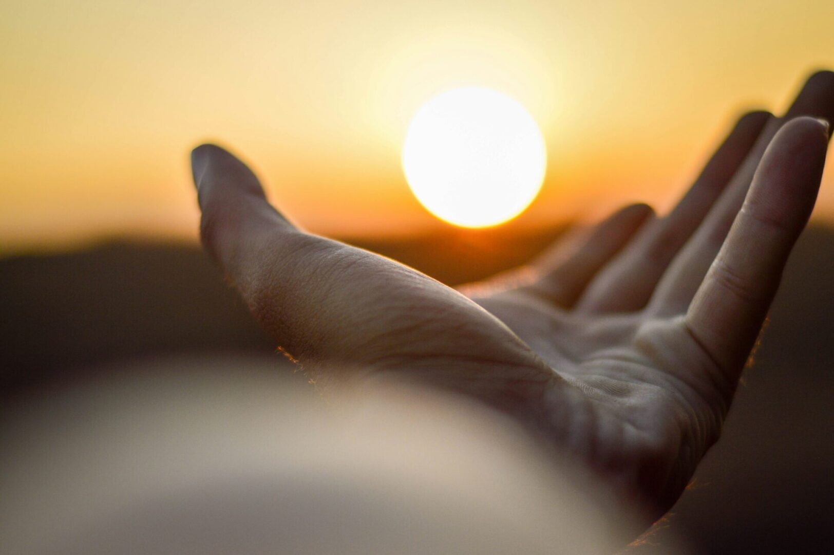 A person 's hand is stretched out in front of the sun.